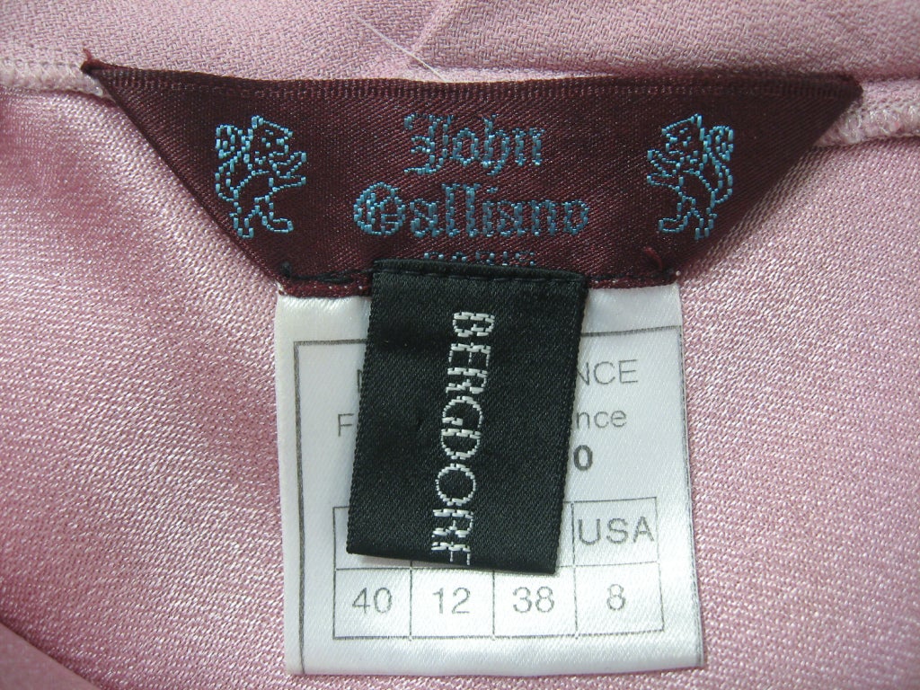 This is an elegant evening gown from John Galliano. It is made of a soft pink acetate and viscose blend fabric and is cut on the bias. There is a v-neck front and a draped open back, is sleeveless and fitted with a mermaid tail hem. There is a