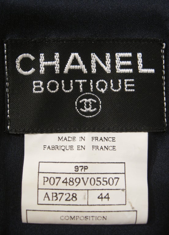 This is a glamorous yet simple style evening gown from Chanel. It is made of a dark navy blue rayon knit that is draped across the bodice and is held in place by a rows of Chanel logo buttons. Zips up the back. High neckline with deep V