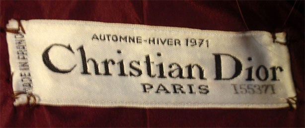 Dies ist ein dreiteiliges Haute-Couture-Ensemble von Christian Dior Haute Couture, aus der Winterkollektion 1971. Es umfasst einen burgunderroten Wollmantel mit zwei offenen, quadratischen Vordertaschen, Fuchspelzkragen und