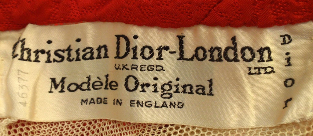 This is a red halter cocktail dress by Christian Dior Haute Couture, from the 1960's. The dress has a matching belt with a bow, black lace detail at the bust , two side slit pockets, a structured bodice with boning, and a layer of tuille and lining