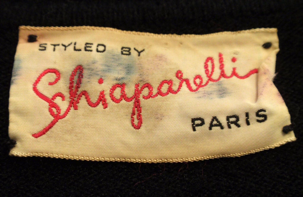 This is a vintage black cashmere sweater with pearl beading by Schiaparelli, from the 1950's. The sweater has nine pearl buttons down the center front, hand beaded flower bouquets, a collar, and ribbed at the waist and cuff.<br />
<br