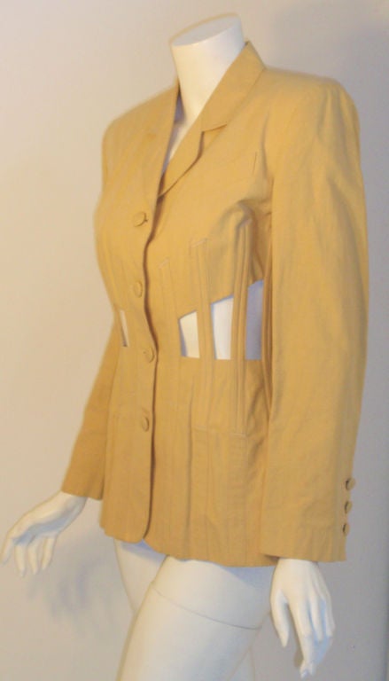 This is a very rare cotton/linen custard jacket by Jean Paul Gautier, from the 1980's. The jacket has open cut outs all around the waist with covered boning detail, four buttons down the center front, shoulder pads, and laces up the center back.<br