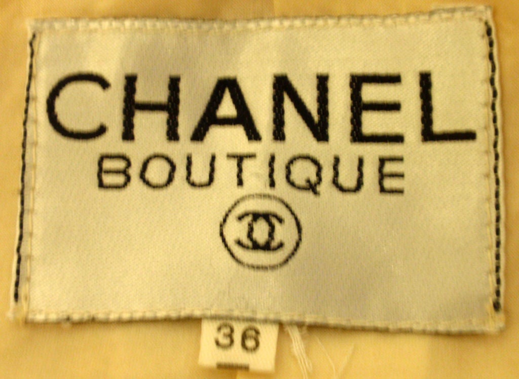 This is a two piece cream wool jacket and skirt set by Chanel, from the 1990's. The jacket has four gold logo 