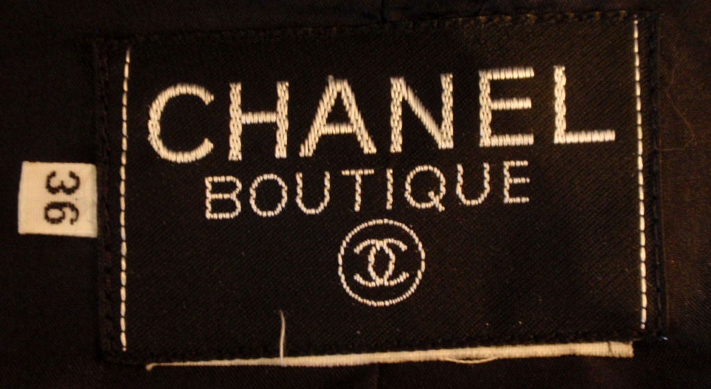 This is a black two piece jacket and skirt set with black silk trim detail by Chanel, from the 1990's. The jacket has gold logo elephant buttons down the front and on the cuffs, four front flap pockets, and a black silk lining.<br />
Size #36<br