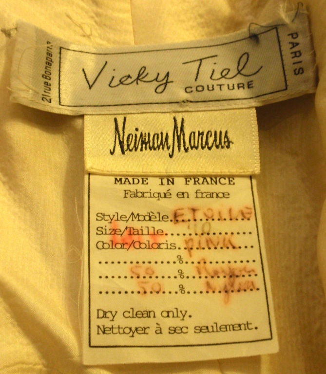 Il s'agit d'une robe bustier en dentelle rose pâle de Vicky Tiel, datant des années 1980. La robe est ornée de perles éparses, d'un corsage construit avec des os, d'une fermeture éclair dans le dos, d'un jupon en satin rose et d'une légère traîne