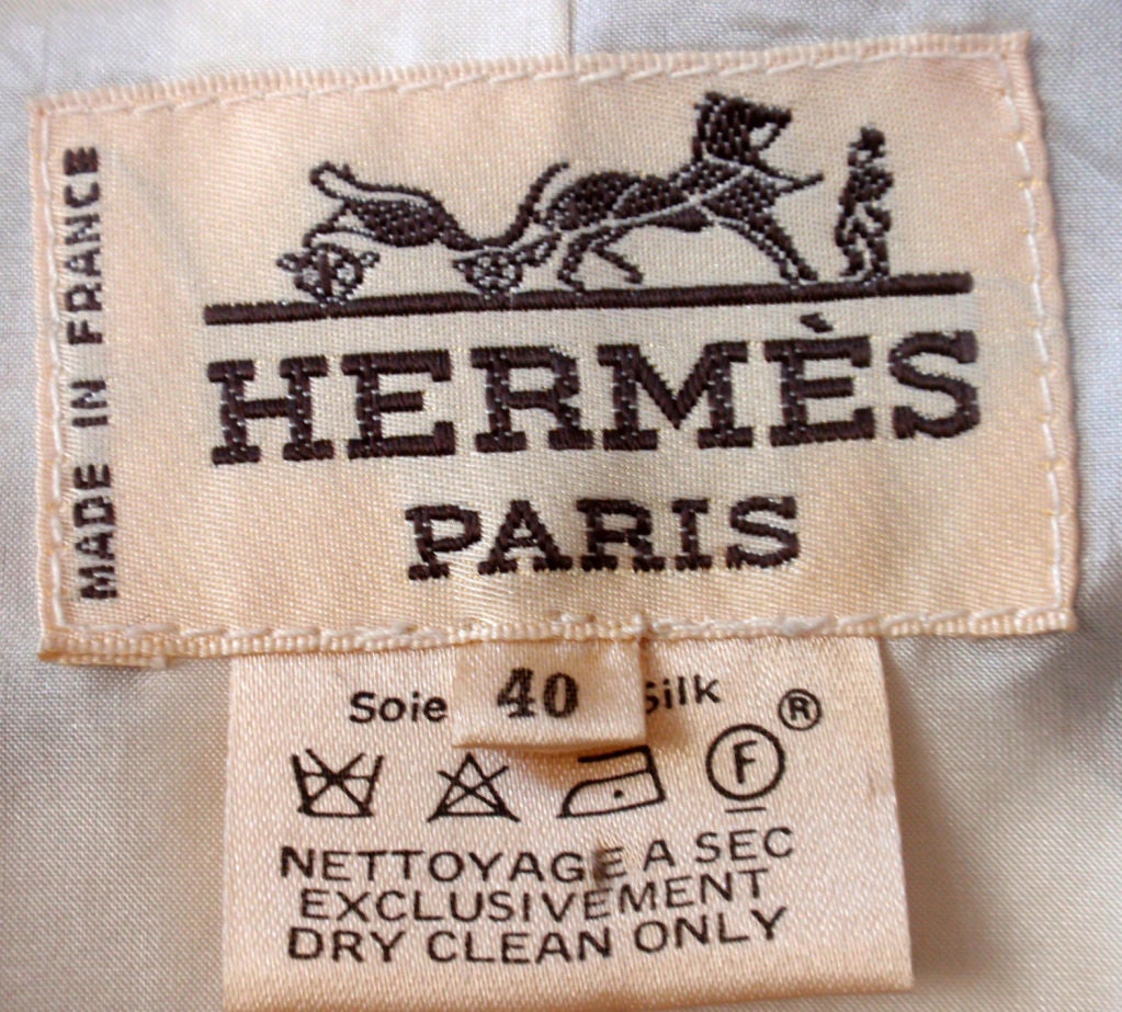 This is a cream silk blouse or jacket with a brown pegasus print by Hermes, from the 1990's. It has nine gold logo buttons down the front and two on each cuff, shoulder pads, a cream silk lining, and four open pockets on the front.<br />
<br