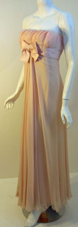 This is a rare vintage light pink peach chiffon gown is attributed to the designer Sarmi, from the 1960's. The gown has feathers all around the bodice, a silk sash and bow, a constructed underpinning bodice, and a zipper up the