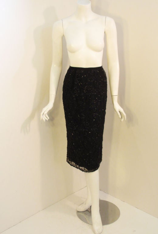 Il s'agit d'une élégante jupe crayon réalisée par Giorgio Sant'Angelo. Il est fait d'une mousseline de soie noire avec des fleurs brodées et perlées, avec du fil lurex noir pour un peu d'éclat. La doublure est en rayonne.

Taille : 10
