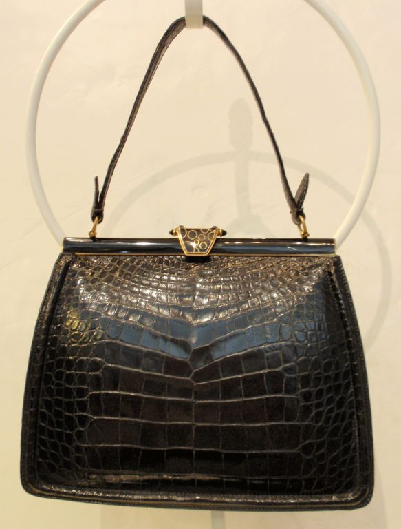 This is a fine vintage alligator skin handbag from Lucille de Paris. There is a single strap and a gold hardware. The clasp on the top has gold circles enameled into it. The interior of this purse is a soft black leather and has 2 pockets, one with