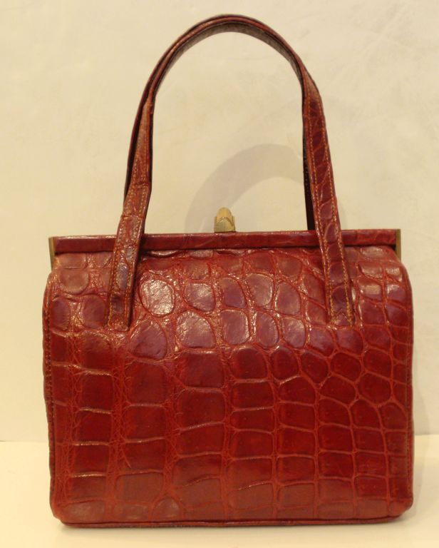 This is a fine red handbag from the 1960's, made out of alligator skin. It is lined in a tan leather, has 2 handles and a snap closure. The interior has 2 open pockets and 2 zippered pockets.<br />
<br />
Measurements:<br />
<br />
Width: 8