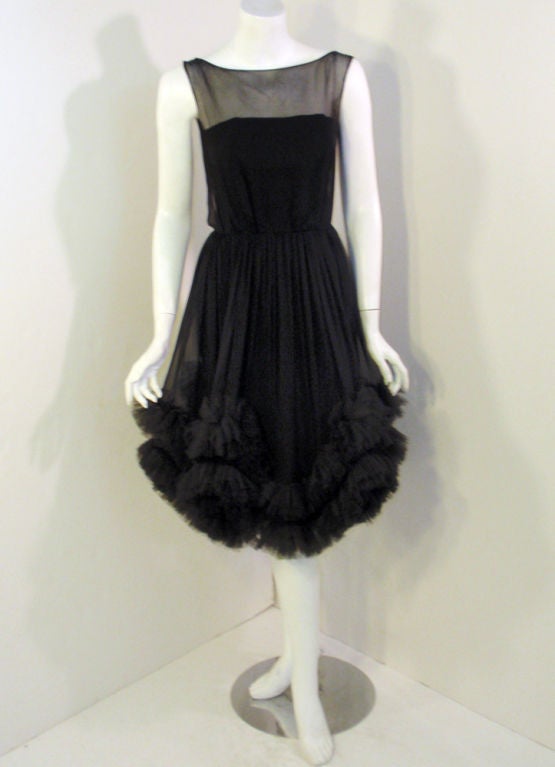 This is a delectable cocktail dress from Ceil Chapman. It is made of a black chiffon with a boned lining, and has rows of tulle ruffles on the edge of the full skirt. The under-dress has a fitted bodice and skirt, with a looser over dress. There is