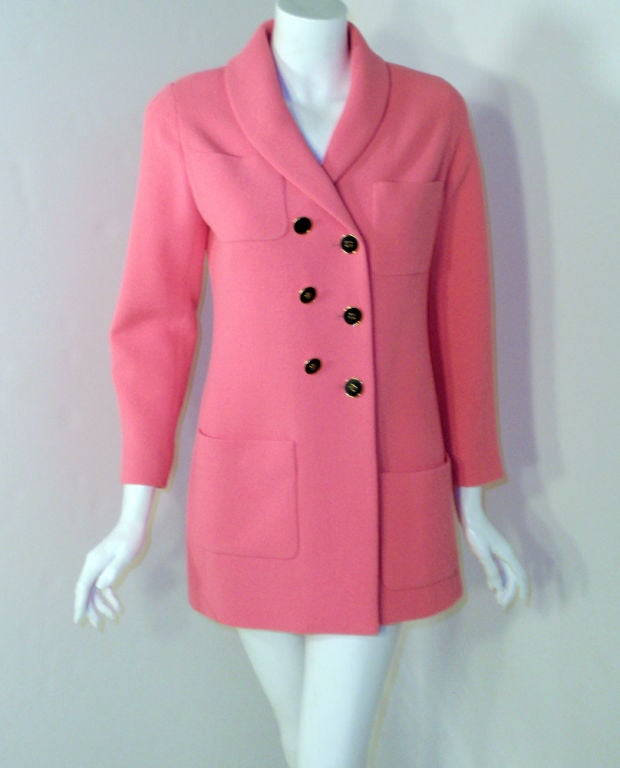 This a cute pink jacket from Chanel. Made with a pink wool, with a matching pink silk lining. The buttons and pockets on the front are sewn on in an asymmetrical fashion. The buttons are black with a gold Chanel logo. It can be worn with a belt, for