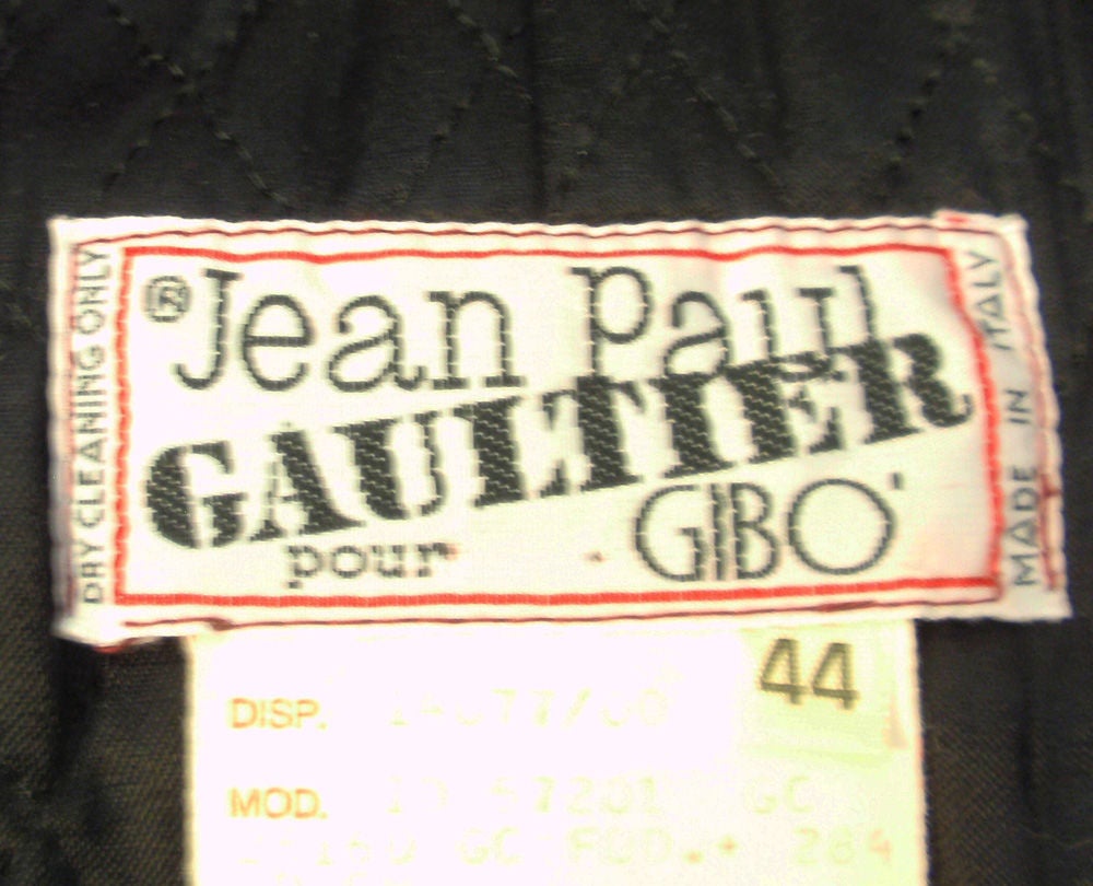 This is a highly collectible skirt suit from Jean Paul Gaultier pour Gibo. It is made of a deep red wool. This ensemble consist of a fitted jacket with 3 large safety pins for the front closures and smaller safety pins on the cuffs in lieu of