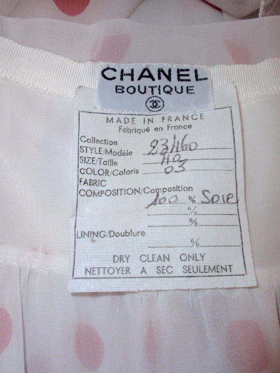 This is an absolutely darling dress from Chanel. It is made of a 100% silk chiffon fabric, with a white with red polka dot print. The dress has a halter style top with a blouson over top, with a shoulder drape and a tie at the neck. The skirt is