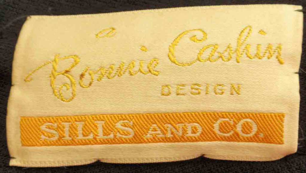 Il s'agit d'un ensemble manteau et jupe en tweed rouge, noir, jaune et orange de Bonnie Cashin, datant des années 1960. Le manteau est doté de garnitures en cuir noir, d'une fermeture à crochets dorés, de deux poches à rabat sur le devant et d'une