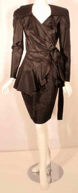 This is a sleek black silk wrap dress by Adolfo, from the 1980's. The dress has long fitted sleeves with zippers at the cuffs, a collar, wraps at the waist with a belt, shoulder pads, and a ruffles at the hip.

Measurements:

Shoulder to