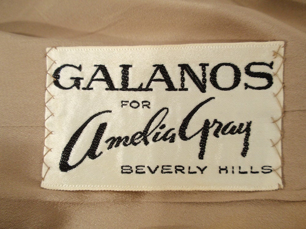 Dies ist ein farbenfrohes Cocktailkleid von Galanos für Amelia Grey. Es ist aus einem rosa, blauen, grauen und braunen Wirbelsatin mit eingewebtem goldenem Lurex-Blumenmuster gefertigt. Es hat einen Reißverschluss auf der Rückseite und ist im