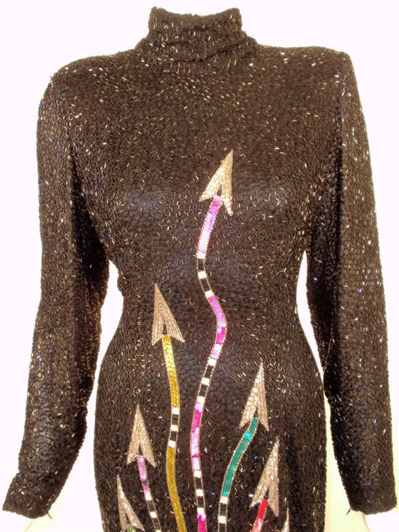 This is a funky evening gown from Bob Mackie. It is fully sequined and beaded on a sheer black fabric and has multi-colored arrows pointing upward from the high low hem. At the hem there are ostrich feather plumes dangling from beaded strips. It