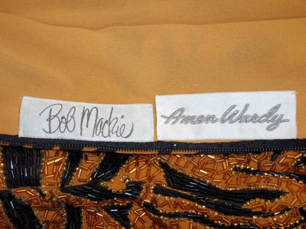 This is an exotic evening gown from Bob Mackie. It is an orange and black long sleeve fitted gown with a tiger print beaded pattern, and a full and flowy chiffon skirt. Fully lined. It zips up the back and at the sleeves, and there are shoulder