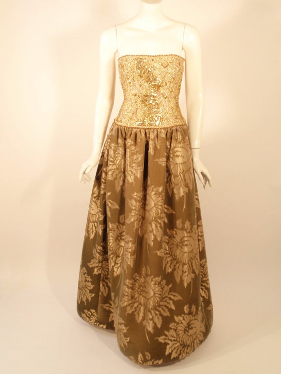 This is an exquisite evening gown from Oscar de la Renta. It is strapless and has a full skirt. The bodice has gold embroidery and beading. There is a built in long line bra and twill tape at the waist for fit. The skirt is a gold and flocked floral