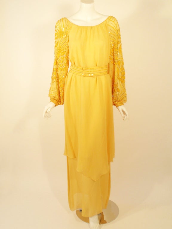 C'est une belle robe de soirée de Rety. Elle est confectionnée en mousseline de soie fluide et présente une silhouette fourreau, avec une jupe à double épaisseur et des manches pailletées et perlées. Il existe une ceinture assortie avec les mêmes
