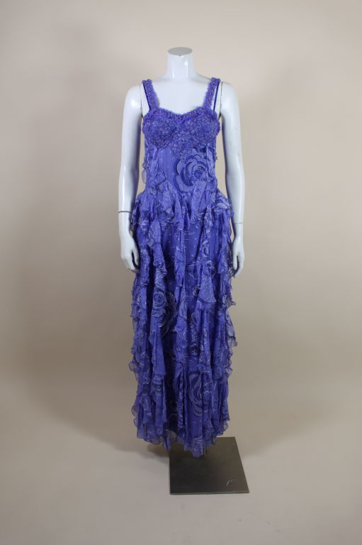 Whimsical chiffon gown from iconic UK designer Zandra Rhodes features her signature silkscreening, this time in a Deco-inspired floral. Dark blue-violet, navy and white blossoms dance across sheer purple chiffon. Bias cut ruffles are stitched on the