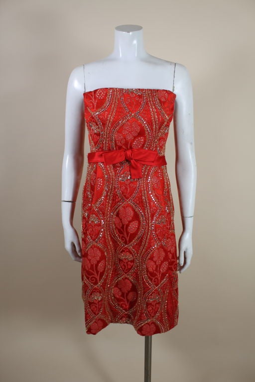 Gorgeous 1960's cocktail dress from American designer Arnold Scaasi is made from a vibrant poppy red and metallic gold brocade. Scrolling floral motif is accented with metallic gold seed beads and textured gold sequins. Fully lined cocktail dress