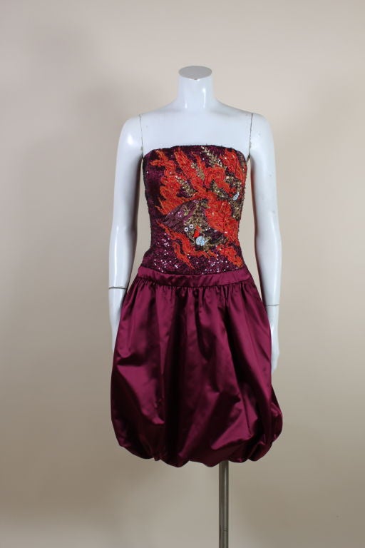 Fabulous cocktail dress from Carolina Herrera features a dramatic Chinese dragon emblazoned across the bodice. Wine red silk satin is covered with iridescent black micro-sequins that surround a dragon vividly embroidered with metallic orange and red