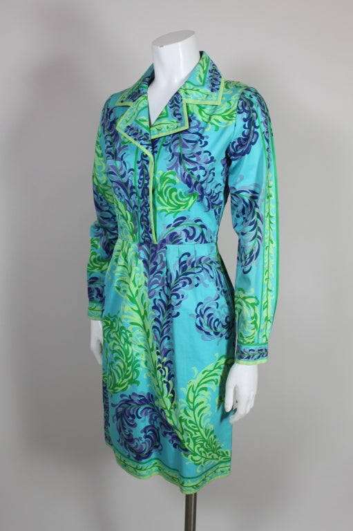 Circa 1960’s Pucci cotton twill dress features a graphic feather plume print in jewel tone shades on a vibrant turquoise background. Dress fastens in the front with a hidden button placket and a side zip. Skirt has crisp pleats at the waist.