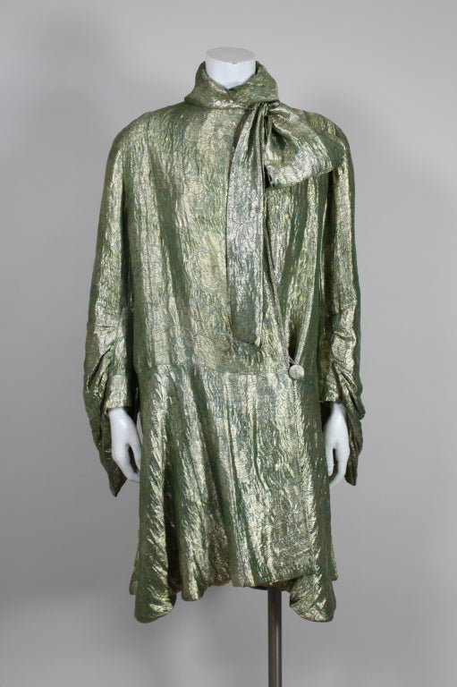 Lovely Art Deco opera coat is made from luxurious metallic silk lamé in moss green shot with gold threads in an undulating lotus blossom pattern. Coat has elegantly draped sleeves that are gathered around a placket and fastens at the collar with an