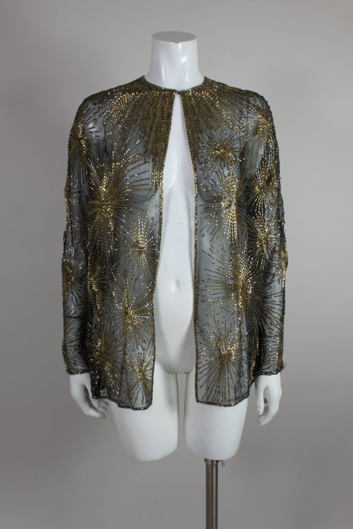 Fantastic chiffon jacket from Halston is beaded with metallic gold and silver firework starbursts. Beading radiates from the neckline like a trompe l'oeil collar. Jacket fastens at the neck with a hook and eye.