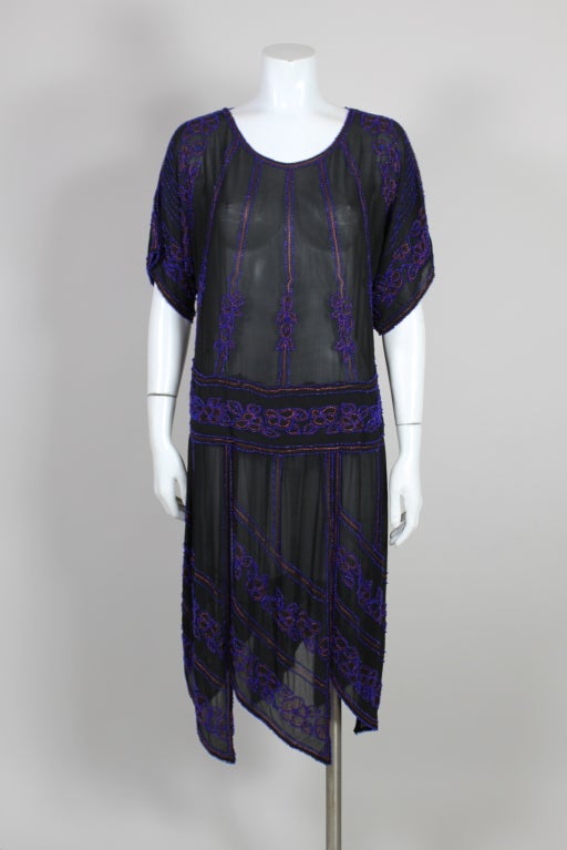 Lovely 1920’s flapper dress is made from black silk chiffon finely embroidered with vibrant cobalt blue glass seed beads. Linear and floral beaded motifs are accented with rust-toned chain stitch embroidery. The skirt is formed from beaded chiffon