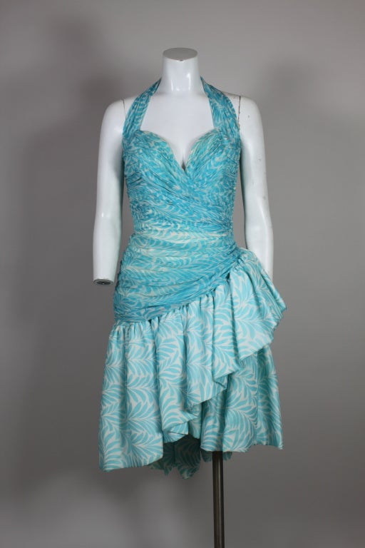 Fun and flirty cocktail dress from couturier Vicky Tiel is made from silk chiffon printed with graphic turquoise vines. Bodice is sculpted with Tiel’s iconic hand tacked pleating to enhance the contours of the body. Skirt is draped with asymmetrical