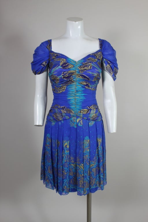 Gorgeous cerulean blue silk chiffon party dress from fashion icon Zandra Rhodes is hand printed with Rhodes' signature whimsical florals in metallic gold and turquoise. Chiffon on the bodice is pleated along a center seam accented with tiny gold