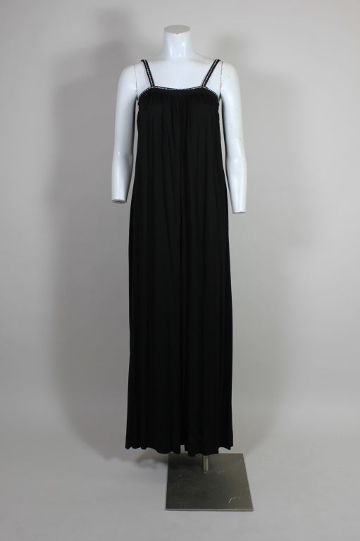 This glamorous, Studio 54 era 1970’s dress from Parisian designer Ted Lapidus is made from lightweight, slinky black jersey. The dress is cut in a trapeze silhouette with rhinestone trimmed neckline and straps. Fastens in the back with a single