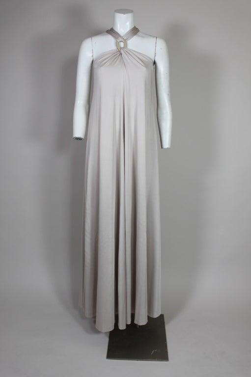 Fabulous 1970's gown from Donald Brooks is done in a slinky dove grey jersey. The neckline is draped in a Grecian style, twisted through two ivory enamel and gold-tone loops (one in front and one in back). 

Measurements--

Bust: 32