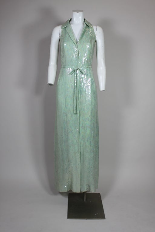 Fabulous 1970's Halston mermaid inspired gown is done in seafoam green silk chiffon covered entirely with iridescent sequins. Gown has a sporty collared neck, hidden snap front closure and a matching belt. Fully lined in chiffon.