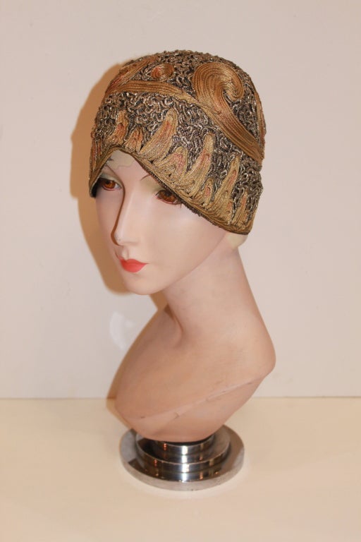 This stunning, hand crafted 1920's cloche is made from net embroidered with metallic lamé threads in shades of silver, gold and copper. A gorgeous swirling motif is embroidered onto the hat in ombré metallics. Rich in texture and color, this hat is