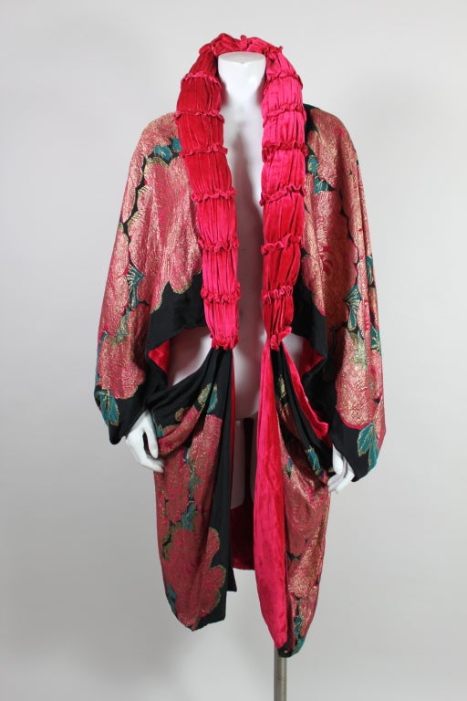 This stunning 1920's Art Deco coat is made from vibrantly colored silk lamé. Giant fuchsia roses cover the body of the coat, woven with metallic gold lamé threads. A sexy cutout is formed in the center by ingenious draping which attaches the lower