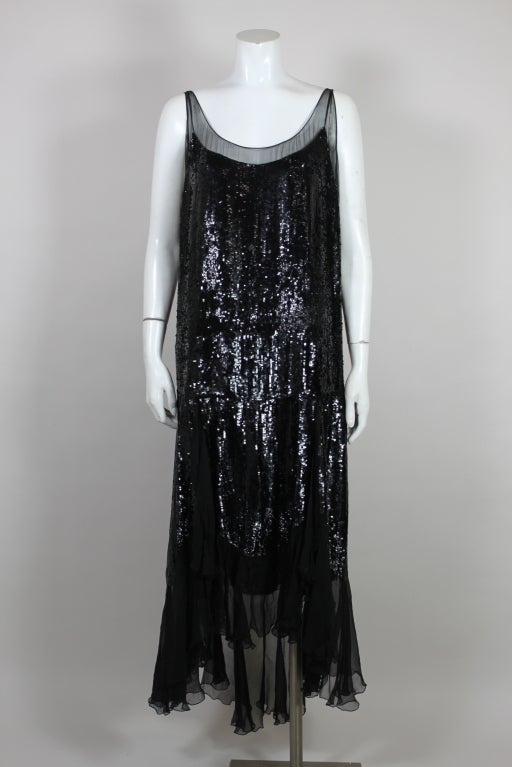 This lovely 1920's flapper dress looks as though its made from liquid metal. Black silk chiffon is covered in rows of shimmering iridescent jet sequins. The dress has a scalloped hem, edged in luxurious ruffles of sheer chiffon.