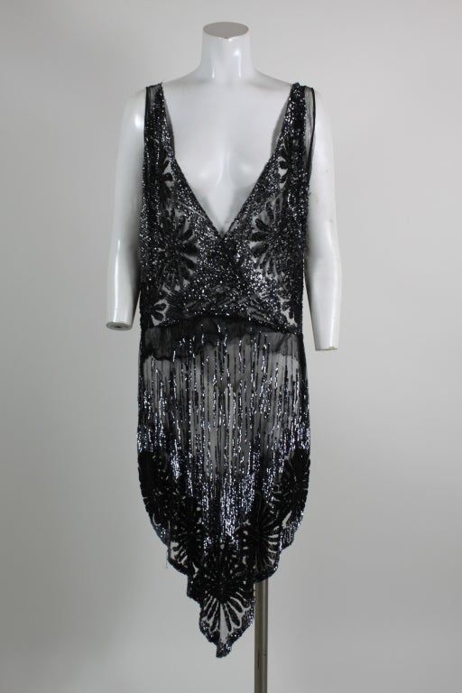 Gorgeous flapper-era dress is made from soft black tulle covered with shimmering, hand sewn sequins and beads. Criss-cross bodice has starburst flowers made from jet bugle beads set in rows of radiating sequins. Asymmetrical hem is decorated with a