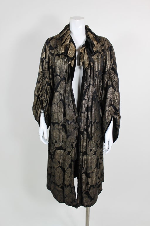 Fantastic 1920's lamé duster coat covered in gold geometric roses and accented with a beautiful petal applique collar. Billowing gathered sleeves give the coat a romantic feel. Lined in black velvet.