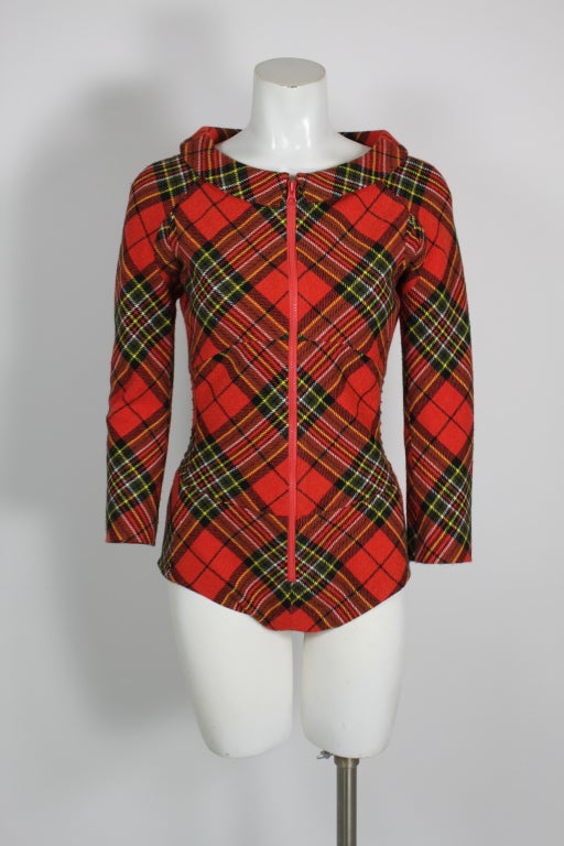 Red and green tartan plaid bodysuit. Red plastic zip front closure with snap closure at crotch. Semi-rounded collar. Gathered at back.