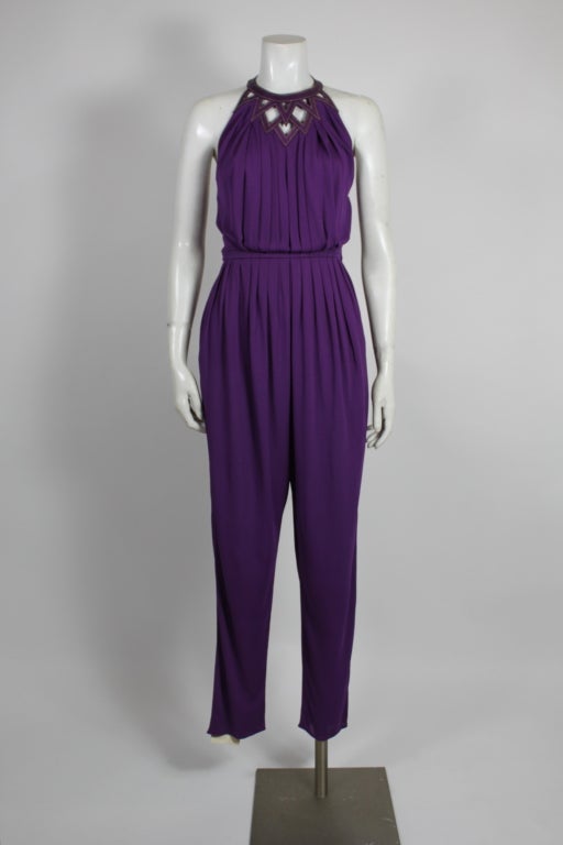 Fabulous jumpsuit by Versace for Genny. Pleating radiates from the waistband adding to the chic halter silhouette. Geometric leather detailing at neck with gold metallic contrast stitching. Jumpsuit comes with purple leather belt (26.25