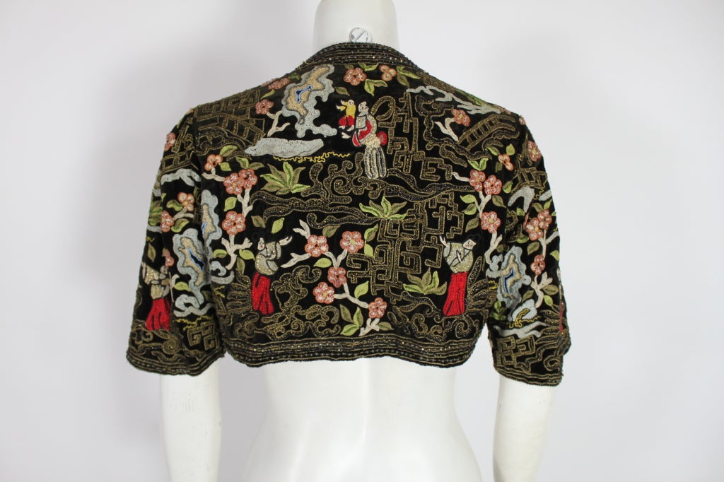 An absolutely stunning example of 1930s craftsmanship, this velvet bolero is covered in vibrant chinoiserie embroidery and beading. The embroidery is of figures in a scene with cherry blossoms and landscape. Embroidery is accented by