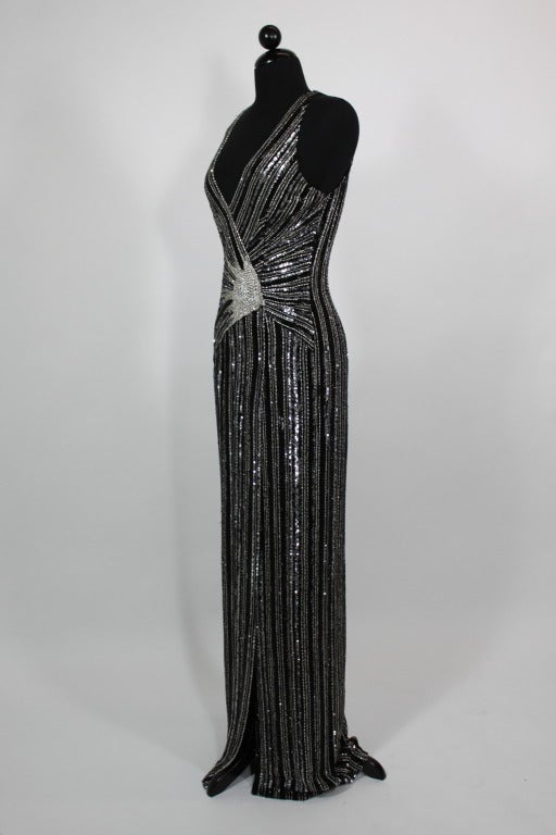 A stunning, densely beaded gown from Balestra done with a modern take on the 1920s flapper silhouette. The slinky gown is covered in black and silver bugle beads as well as a starburst cluster of rhinestones at the waist. 

Gown zips in back and