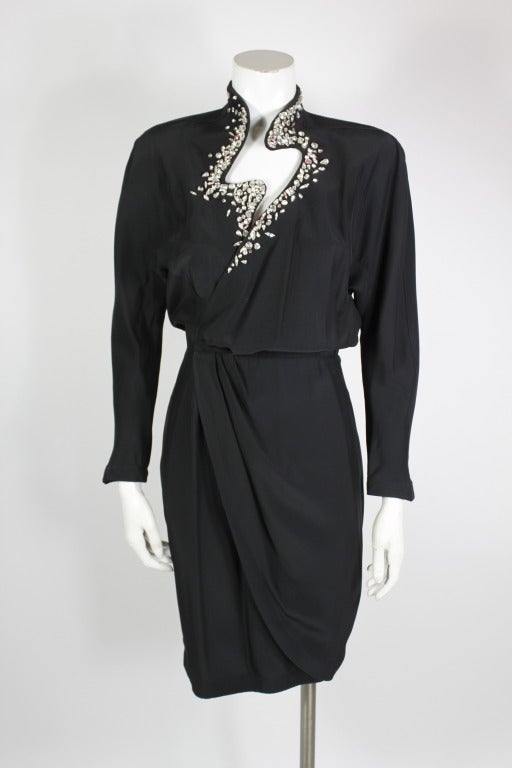 Always with an eye toward the unexpected, Thierry Mugler created this black wrap cocktail dress with a striking asymmetrical cutout, lined with white and light pink rhinestones in varying shapes and sizes. Structured shoulders. Mandarin collar.