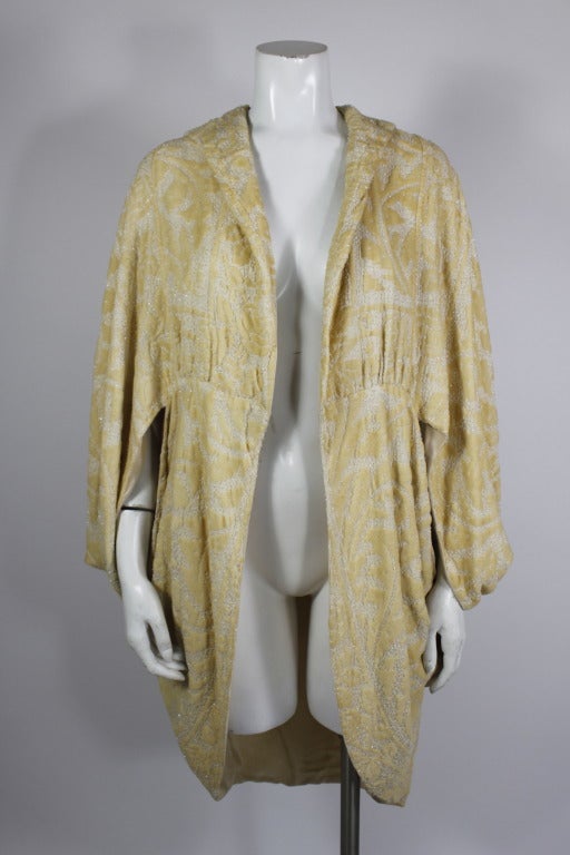 A luxe, gorgeous cocoon jacket from the 1920s. Done in an eggshell cut velvet floral motif and embellished with beads. The back of the jacket has a mock hood complete with a beautiful beaded tassle that hangs down. Fully lined.