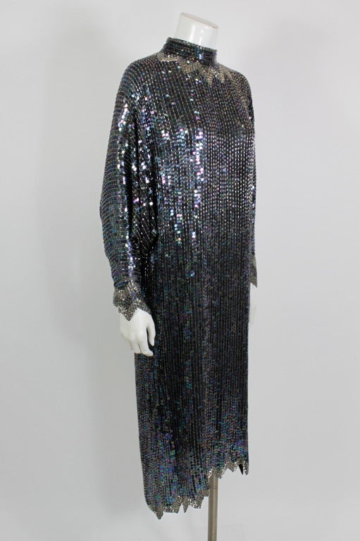 Classic sequined cocktail dress from Halston. Alternating columns of black iridescent sequins and bugle beads cover the dolman-sleeved cocktail dress. Finished with an asymmetric hem bordered in contrasting silver beads.  Backed by silk chiffon.