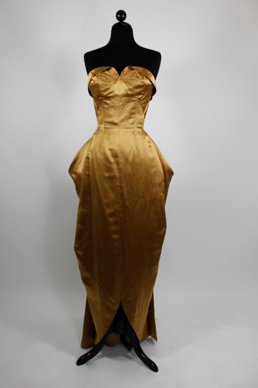 An incredible architectural 1950s strapless gown. Done in a rich copper satin, the gown is draped beautifully and elegantly. Complete with a stunning nipped waist, the skirt is structured with exaggerated hip flounces and a slight train in